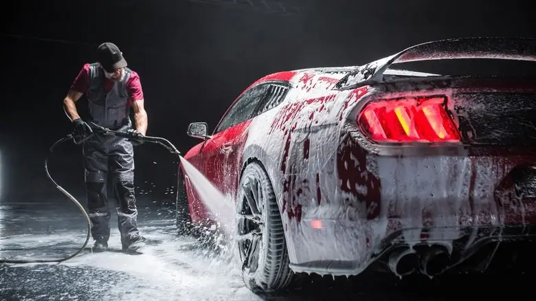 A technician rinsing foam from the rear of the Mustang mid-detail